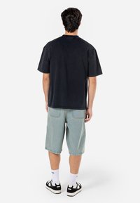 T-shirt en coton oversize noir, associé à un short en denim bleu clair. Le modèle porte des baskets noir et blanc avec des chaussettes blanches. Design simple.
