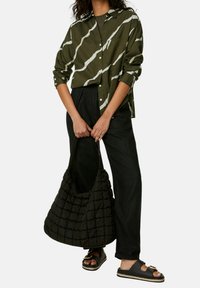 Olijfgroene shirt met witte golvende strepen, zwarte losse broek, een zwarte gewatteerde tas en zwarte instapsandalen met een metalen accent.
