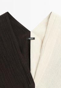 Close-up van een kledingstuk met zwarte en witte geribbelde stofsecties die aan de kraag zijn verbonden, met een Massimo Dutti-label.