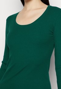 Grön, ribbad långärmad topp med en rundad halsringning. Tyget har en jämn struktur med stretch och en figurnära silhuett.