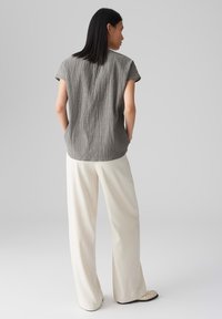 Blusa grigia con texture e maniche corte, abbinata a pantaloni bianchi a gamba larga. La parte superiore presenta un sottile motivo verticale e un orlo rotondo.