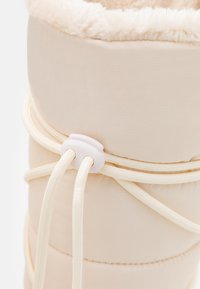 Helle beige gepolsterte Stiefel mit einem weichen, flauschigen Innenfutter. Verfügt über ein strukturiertes Äußeres, elastische Schnürsenkel und einen weißen Kunststoff-Stopper zur Anpassung.