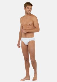 Weiße Baumwollunterwäsche mit nahtlosem Design, weicher Textur und elastischem Bund, präsentiert von einem stehenden männlichen Modell.