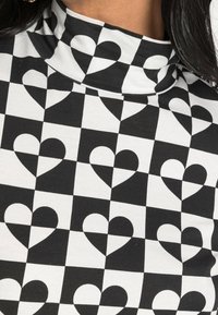 Svart och vit höghalsskjorta med ett rutmönster som har växlande hjärtformer. Tillverkad av ett mjukt, elastiskt tyg.