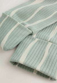 Mangas de punto acanalado en verde claro con rayas blancas verticales, extendidas sobre una superficie pálida, mostrando detalles del puño y la textura de la tela.
