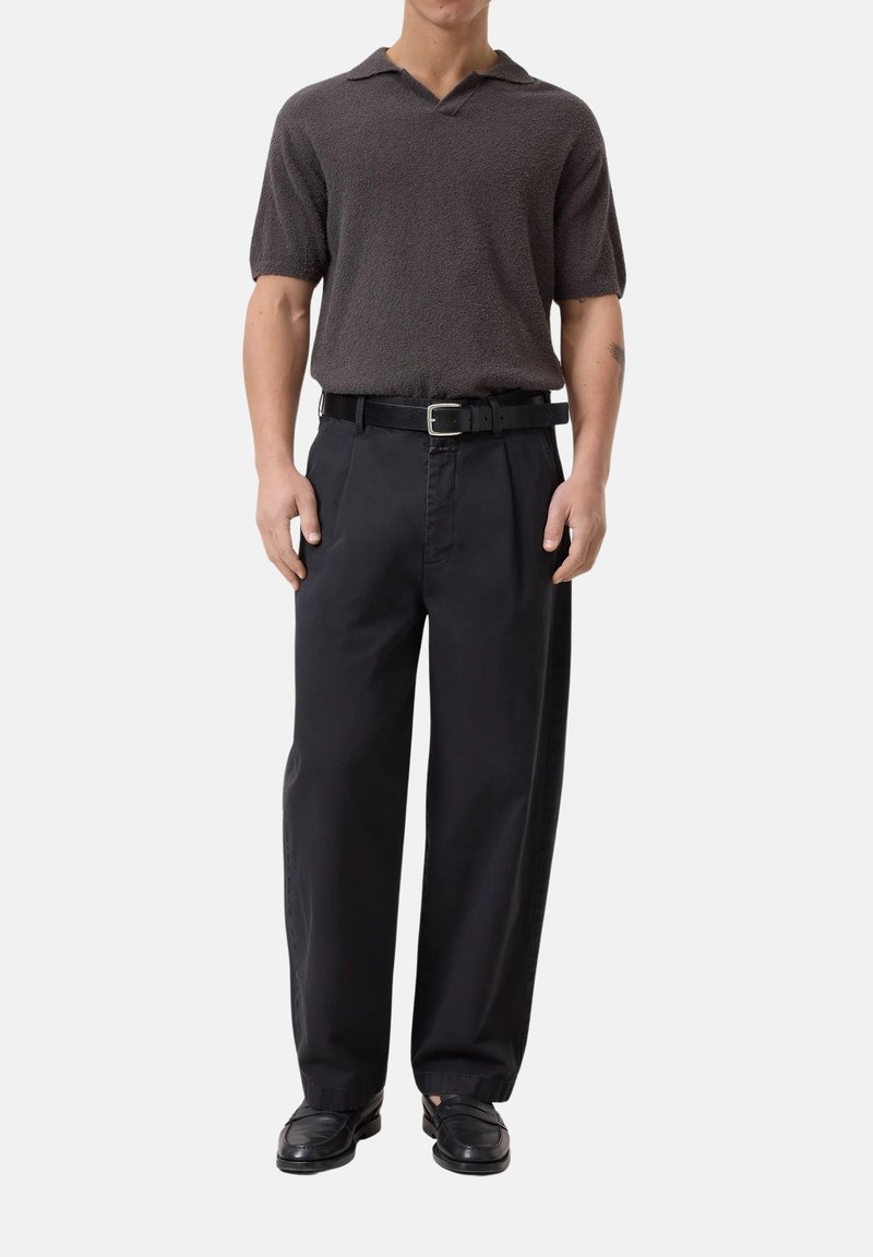 Polo a maniche corte, marrone scuro, con texture e scollo a V, abbinato a pantaloni neri a vita alta e gamba larga, con una cintura nera.