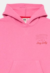 Hoodie rosa feito de tecido suave, com um bolso frontal, capuz com cordão e o logótipo "ROXY 90 Stay Salty" em rosa mais escuro.