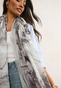 Lightweight grey scarf featuring a textured, patterned design with various shades and scattered metallic accents. Drapes softly.