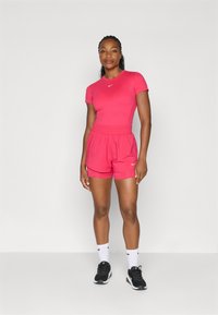 Top atlético rosa ajustado y pantalones cortos a juego, ambos hechos de material ligero. Presenta el logo de Nike en blanco. Zapatillas de correr negras y calcetines blancos.