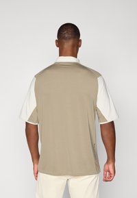 Polo à manches courtes avec un dos beige et des manches blanches ; fabriqué à partir d'un tissu lisse avec une texture subtile et un col.
