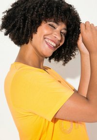 T-shirt jaune à manches courtes avec un col rond, présentant un design texturé sur le devant et une texture de tissu lisse.