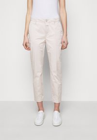 Pantalons beige clair de longueur cheville en mélange de coton, avec une fermeture à bouton et deux poches latérales, associés à des baskets blanches.