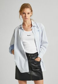 Svetlomodrá a biela pruhovaná košeľa s gombíkmi cez biely tielko s logom "Pepe Jeans", doplnená čiernou sukňou z faux kože s zipsom.