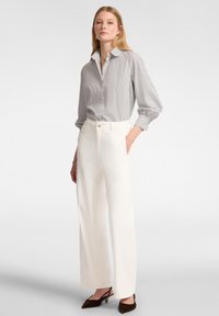 Camicia a righe con maniche lunghe, abbinata a pantaloni bianchi a vita alta. Scarpe in broccato con punta affusolata completano l'outfit.