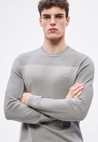 Pulover gri cu mâneci lungi, cu dungi, și decolteu rotund. Prezintă un logo subtil BOSS pe piept, textură fină și design ajustat.