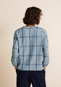 Ljusblå rutiga topp med långa ärmar, rund halsringning och kontrasterande blå och krämfärgad rutig mönster. Mjuk tyg med en avslappnad passform.