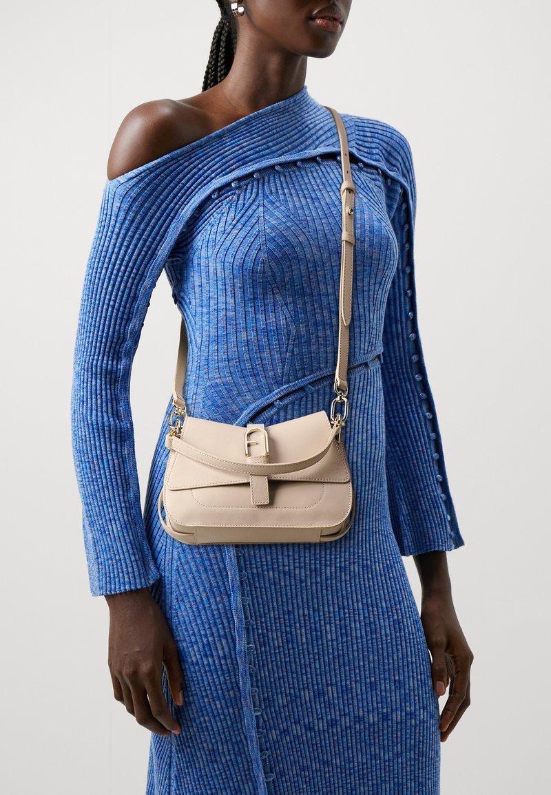 Beige leather crossbody bag with a flap, buckle closure, and metal hardware. The bag has a smooth texture and a rectangular shape.