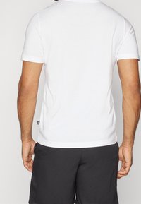 Camiseta blanca de manga corta con cuello redondo, textura suave y una pequeña etiqueta negra en el lateral, combinada con pantalones cortos oscuros.