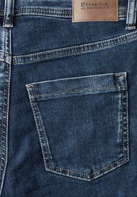 Jeans de mezclilla de color azul oscuro, con un bolsillo trasero, costuras claras en contraste y una etiqueta rectangular de cuero en la cintura.