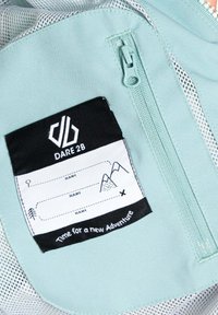 Mintgrüner Stoff mit einem schwarzen Etikett, das das "DARE 2B"-Logo, Platz für Namen und Abenteuergrafiken zeigt. Zipperdetails sind sichtbar.