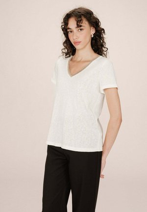 T-shirt bianco a V con maniche corte, caratterizzato da un collo testurizzato e una vestibilità ampia, abbinato a pantaloni neri. Tessuto dalla consistenza liscia.