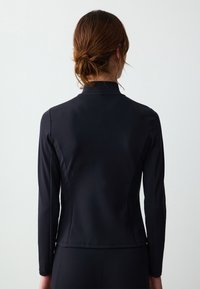 Giacca nera a maniche lunghe realizzata in tessuto elastico e liscio. Presenta un colletto alto e una silhouette aderente, con dettagli di cucitura lungo la schiena.