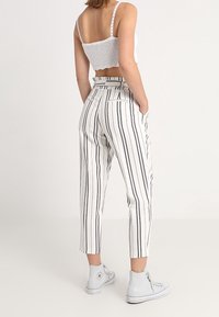 Bílé, vysoké pruhované kalhoty s přiléhavým střihem, s vertikálními černými pruhy, postranními kapsami a zkrácenou délkou.