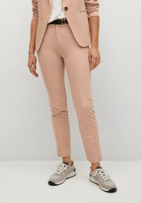 Pantalon rose clair sur mesure, coupe slim, associé à une chemise blanche et des baskets grises. Tissu lisse et design minimaliste.