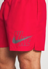 Piros Nike rövidnadrág elasztikus derekkal, az alsó bal oldalon egy szürke logóval. Az anyaga simának és könnyűnek tűnik.