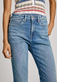 Vaqueros de mezclilla en azul claro con un ajuste Slim, que presentan un diseño clásico de cinco bolsillos, un sutil desgaste en la tela y una cintura de altura media.