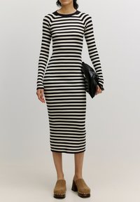 Schwarz-weißer gestreifter, gerippter Strickkleid, lange Ärmel, figurschmeichelnde Silhouette, knielang, kombiniert mit einer schwarzen Clutch und beigen Absatz-Mules.