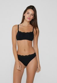Černá souprava spodního prádla obsahující top s krajkovým lemováním a nastavitelnými ramínky, doplněná o odpovídající bikiny s krajkovými akcenty. Měkká tkanina.