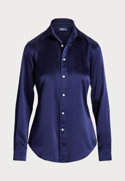 Temno modra satenasta srajca s kratkimi rokavi, s koničastim ovratnikom in belimi gumbi. Gladka tekstura in klasičen kroj.