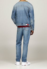 Jeansjacka och jeans i ljusblått med manchesterkrage och slitna detaljer. Vita skor med röda och blå logotypdetaljer.