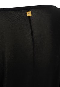 Tunic nera in maglia con una finitura testurizzata, caratterizzata da una cucitura verticale e un piccolo tag dorato vicino al colletto.