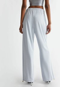 Pantaloni larghi di colore azzurro chiaro realizzati in un tessuto lucido, con una cintura elastica e piccoli dettagli dorati all'orlo. Texture liscia.