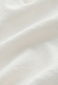 White fabric with subtle crinkle texture and soft folds creating gentle shadows across the surface.