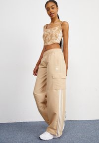 Μπεζ cropped top με διακριτό σχέδιο, συνδυασμένο με χαλαρές μπεζ cargo παντελόνες που διαθέτουν λευκές πλαϊνές ρίγες και μια πλαϊνή τσέπη. Λευκά sneakers.