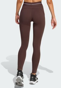 Brown leggings with a smooth, stretchy texture and high waistband, featuring subtle stitching details, paired with black athletic shoes.