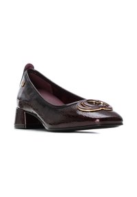Zapato plano de charol burdeos con un tacón bajo tipo bloque, que presenta un acento de logo dorado en la puntera y un acabado texturizado.