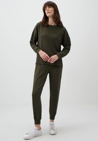 Completo di felpa e pantaloni in verde oliva, con maglia a maniche lunghe a vestibilità larga e pantaloni a gamba affusolata con polsini. Abbinalo a sneakers bianche. Texture morbida.