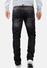 Zwarte denim jeans met een vervaagde wassingen, voorzien van versterkte knieregios, gestikte achterzakken en logo-details op de tailleband.