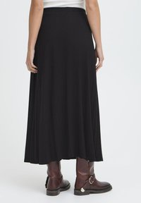 Črna maksi krila v lahkem dizajnu, izdelana iz mehkega materiala. Ima gladek pas in sega do gležnjev, v kombinaciji s svetlo rjavimi gležnjači.