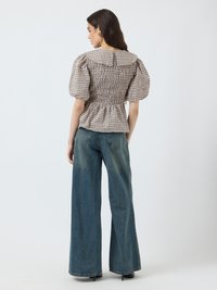 Brown and white checkered puff-sleeve top with a large collar, gathered smocked back, paired with high-waisted wide-leg blue jeans.