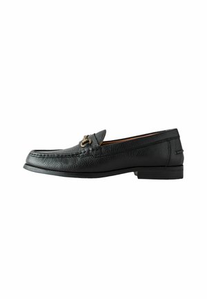 Mocassin pour homme en cuir noir avec une boucle métallique dorée, bout mocassin, et petit talon empilé, présenté de profil sur fond blanc.