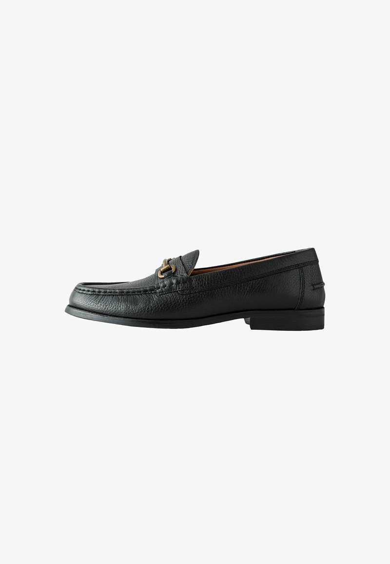 Mocassin pour homme en cuir noir avec une boucle métallique dorée, bout mocassin, et petit talon empilé, présenté de profil sur fond blanc.