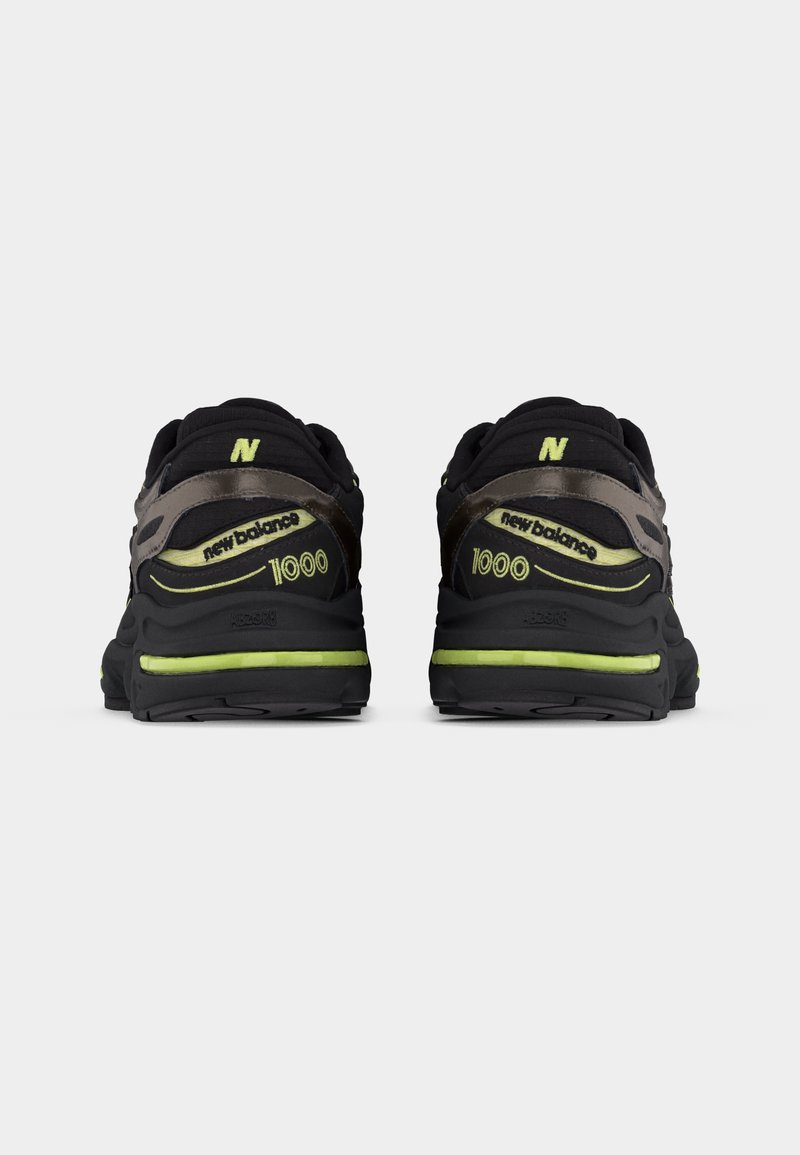 Par de zapatillas New Balance 1000 negras y grises con detalles en verde neón, vistas desde atrás sobre un fondo blanco liso.