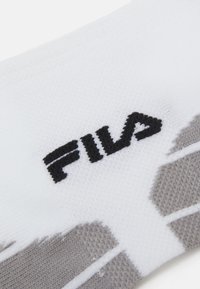Chaussette blanche avec un logo "FILA" noir, un tricot texturé, des accents gris et des motifs distincts à l'extérieur.