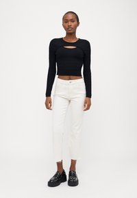 Black ribbed long-sleeve cropped top with a front cutout, paired with white straight-leg pants and black platform shoes with silver studs.