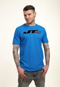 Blaues Baumwoll-T-Shirt mit einem großen schwarzen und roten "JT Racing"-Logo auf der Brust. Kurze Ärmel und runder Ausschnitt.